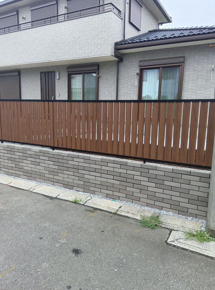 埼玉県坂戸市の施工事例｜道路側からの引きで、木調の横格子フェンスとグレーのタイル壁が一直線に伸びる構図